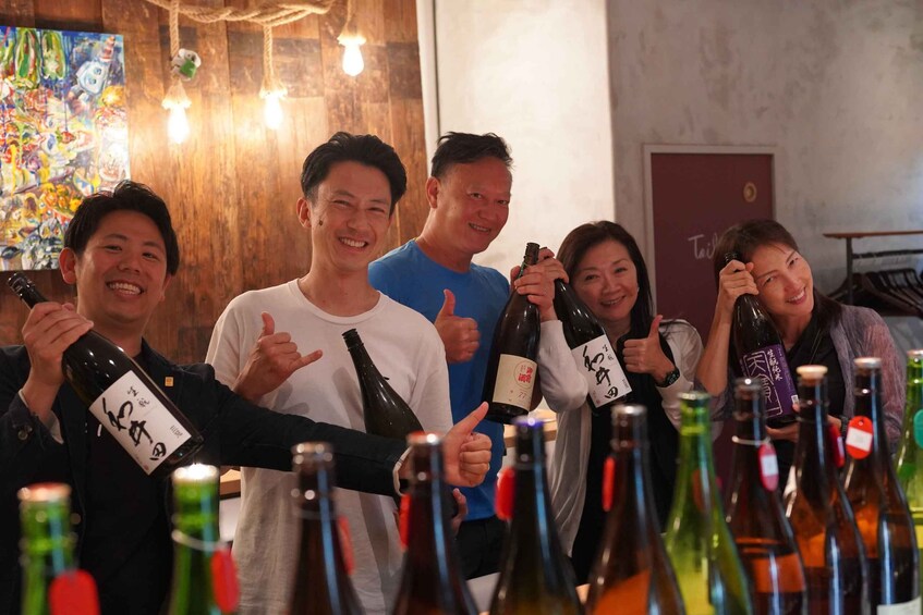 A group of people holding wine bottles with labels, standing in a room with wooden walls and a colorful painting in the background. 5