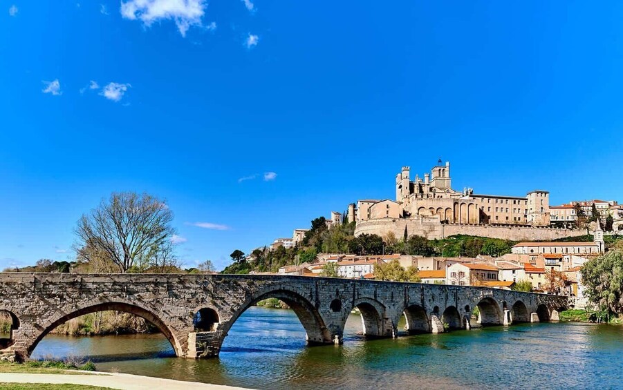 A stone bridge over a river, a historic building on a hill, and clear blue sky. 1