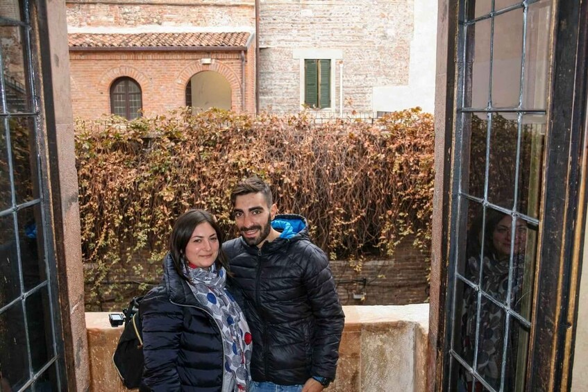 A couple standing in an outdoor area with brick buildings and a hedge in the background. 4
