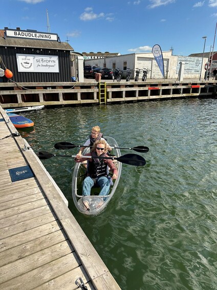 A person in a kayak on a body of water, a wooden dock, and a building with signage. 4