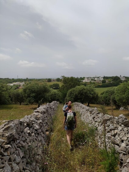 A person walking along a stone wall in a rural area with greenery and buildings in the background. 4