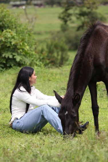 A person sitting on grass with a horse grazing nearby. 1
