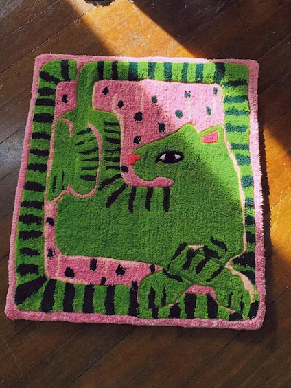 A square rug with a green and pink crocodile design on a wooden floor. 4