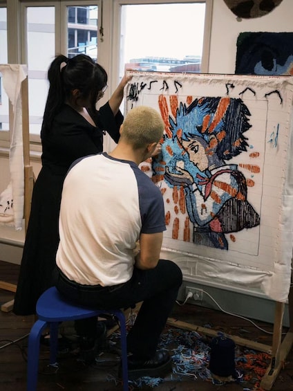 Two people working on a large tapestry with a colorful design. 3