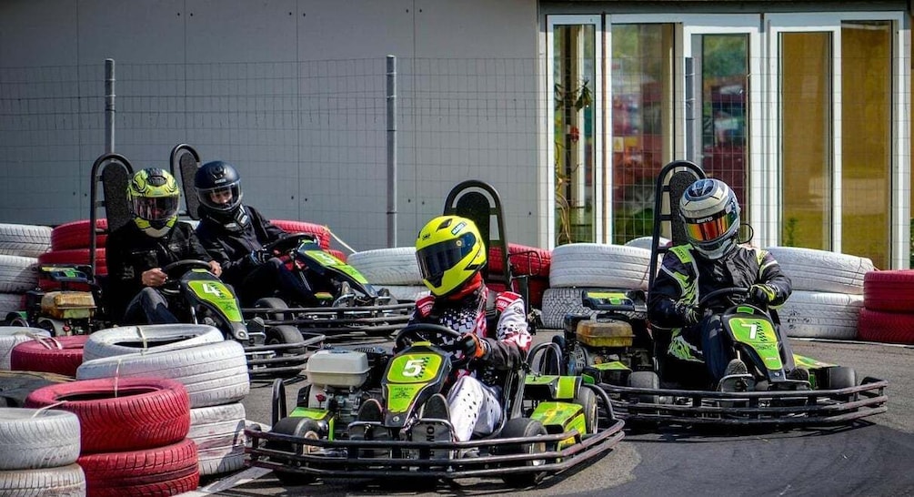 Go-karts with drivers in racing suits and helmets, lined up with racing tires. 4