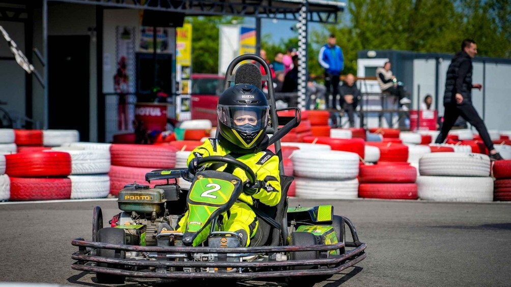 A go-kart racer in a yellow suit with the number 2, driving on a track with red and white barriers. 3
