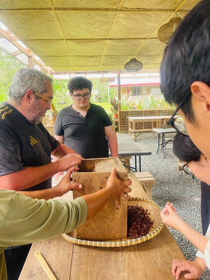 A group of people at an outdoor market, examining a wooden box with a woven basket containing coffee beans. 4