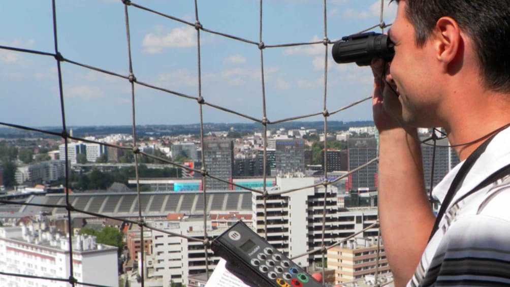 A person using binoculars, holding a remote control, with a cityscape in the background. 5