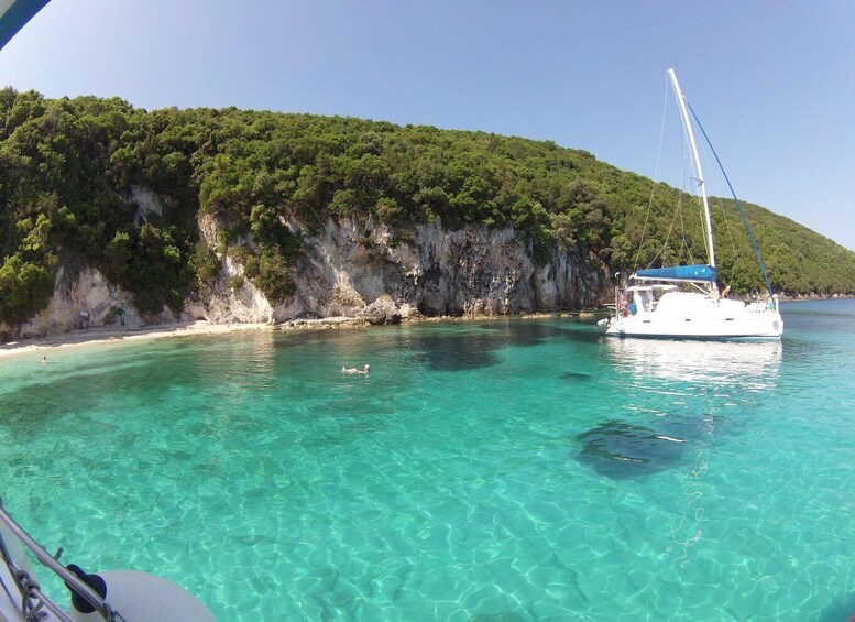 A boat on clear turquoise water, a sandy beach, and a forested cliff. 2