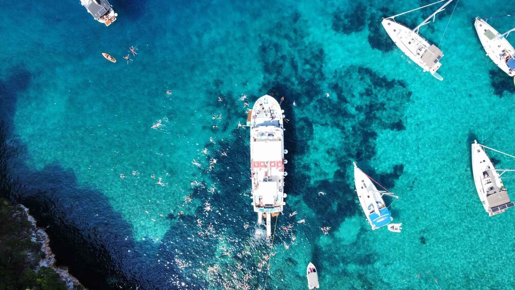 A large cruise ship surrounded by smaller boats in clear turquoise waters. 3