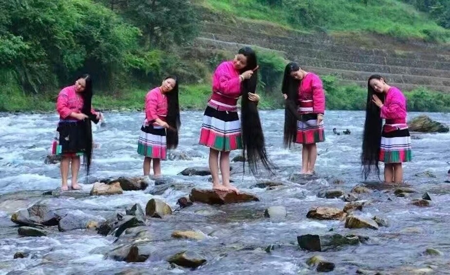 A group of people in traditional attire standing on rocks by a flowing river. 5