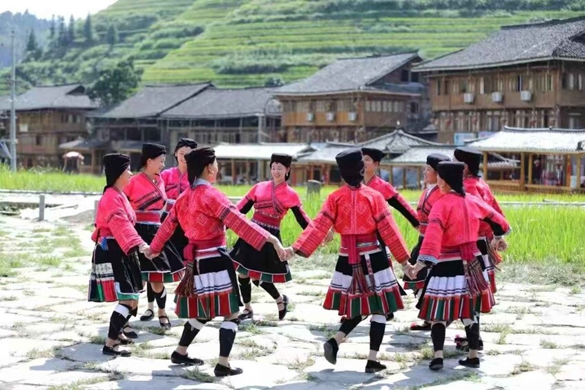 A group of people in traditional attire performing a dance in an outdoor setting with buildings in the background. 2