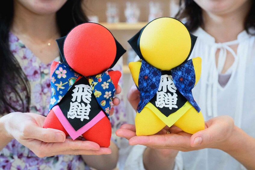 Two people holding small figures with red and yellow heads, and black and blue clothing. 1