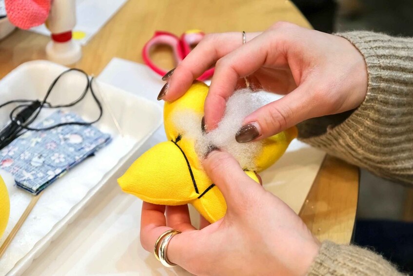 Hands holding a yellow object with a black line, possibly a toy or model, with a white fluffy substance on it. 5