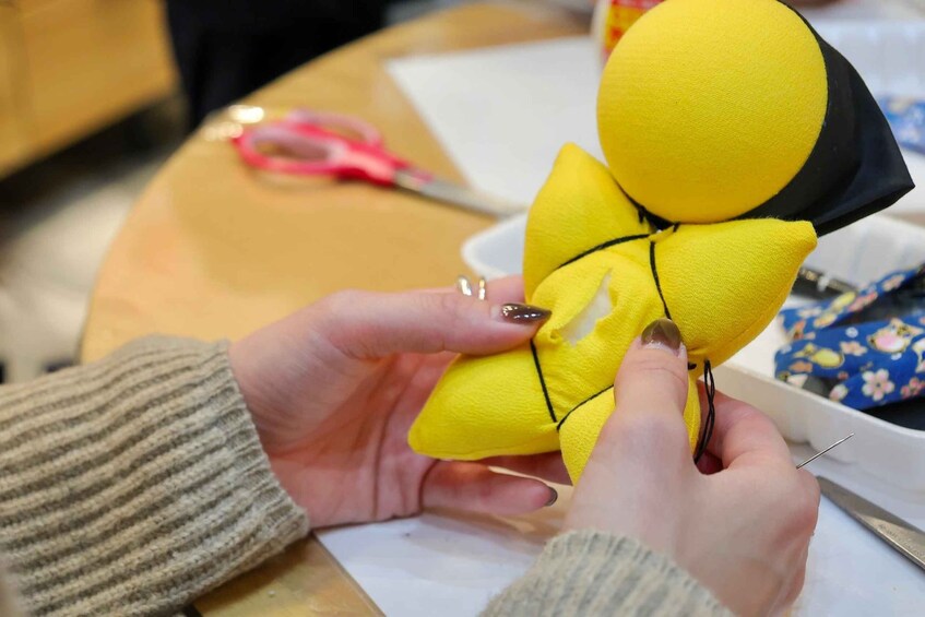 Hands holding a yellow object with black details, possibly a toy or craft. 5