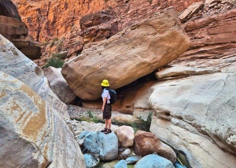 A person hiking in a rocky canyon with large boulders and red rock formations. 5