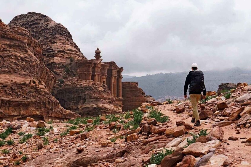 A person hiking on a rocky trail with a historical building in the background. 3