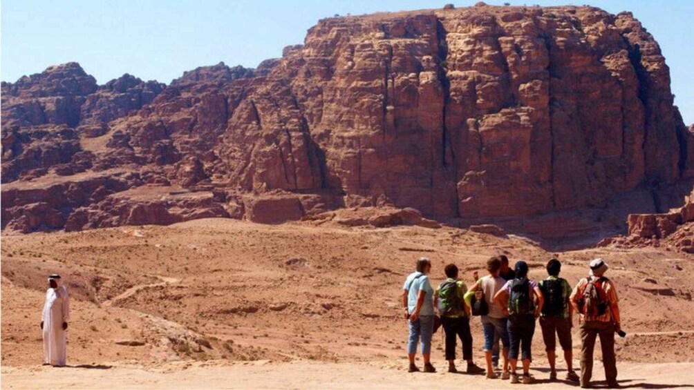 A group of hikers on a desert trail with a large rock formation in the background. 2