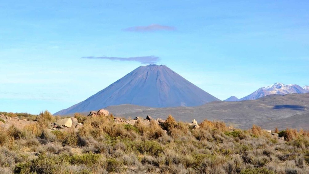 A volcano with a plume of smoke, surrounded by a dry, grassy landscape and distant mountains. 5