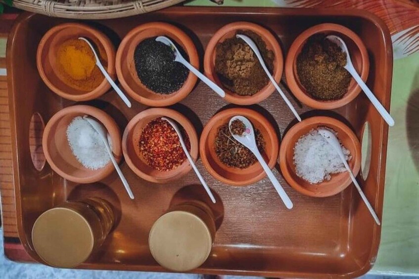 A tray with multiple small clay bowls containing different spices and two small containers of liquid. 2