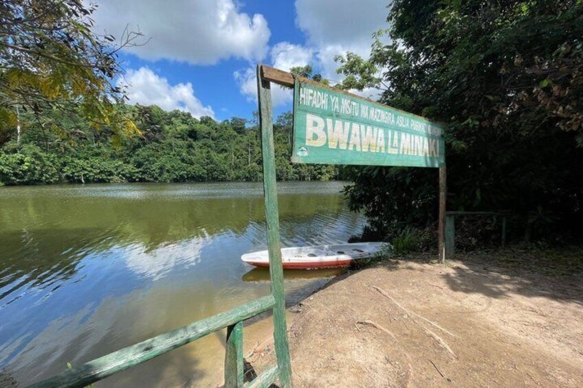 A river with a sign reading 'Bwawa La Minaki' and a paddleboard in the water. 5