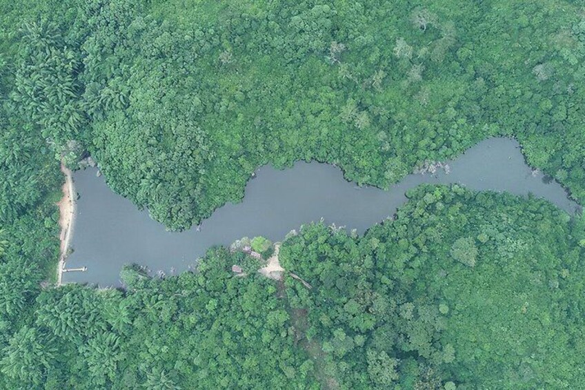 A river winding through dense green forest with a small bridge and a dirt path. 2