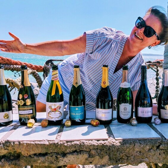 A person leaning on a table with various wine bottles in a coastal setting. 4