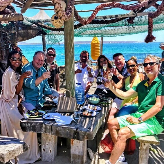 A group of people toasting at a wooden table with a view of the sea. 3