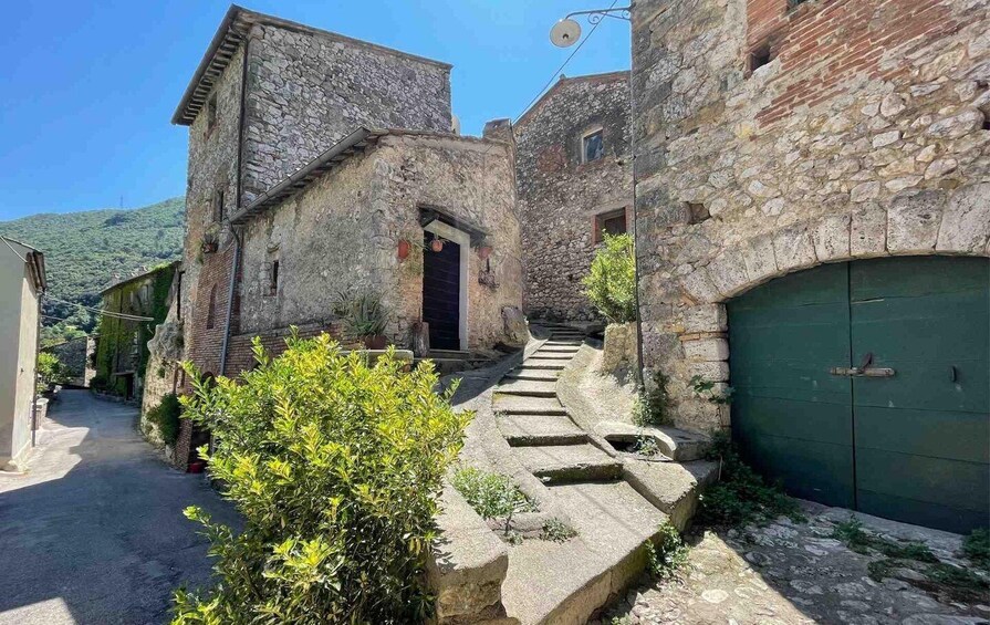 A narrow stone pathway leading to a building with a dark door, flanked by greenery and stone walls. 3