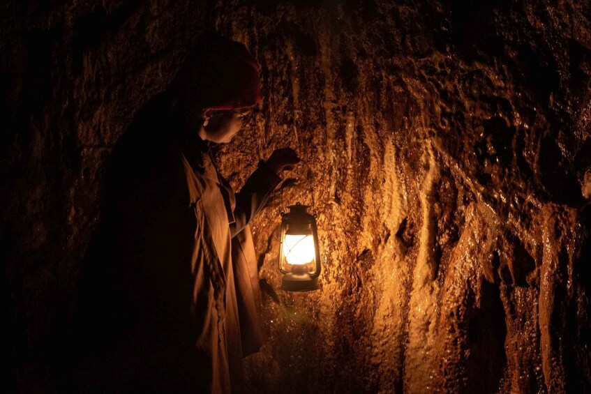 A person in a cave with a flashlight illuminating the rocky walls. 1