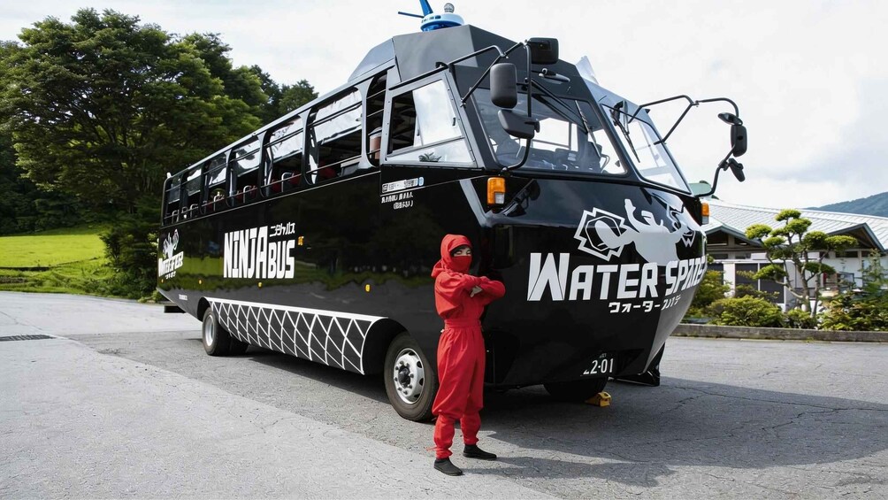 A black bus with 'NINJABUS' and 'Water Spree' written on it, parked on a road with a person in red standing beside it. 1