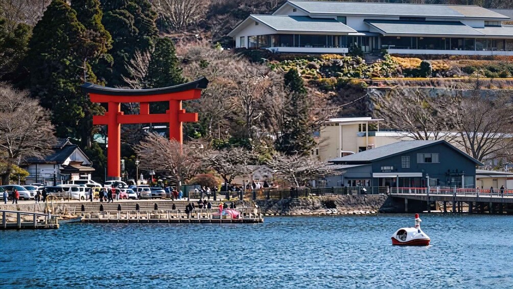 A red torii gate, a body of water, a small boat, and buildings in the background. 4