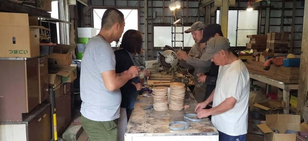 A workshop with people working on a table, surrounded by boxes and tools. 1