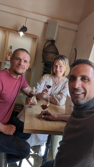 Three people sitting at a wooden table with wine glasses. 4