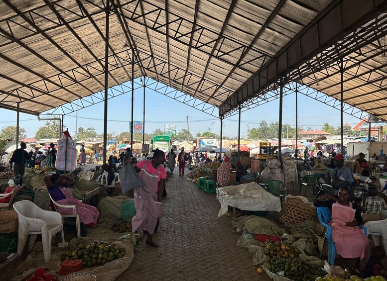 An outdoor market with vendors selling fruits and vegetables under a metal roof. 1