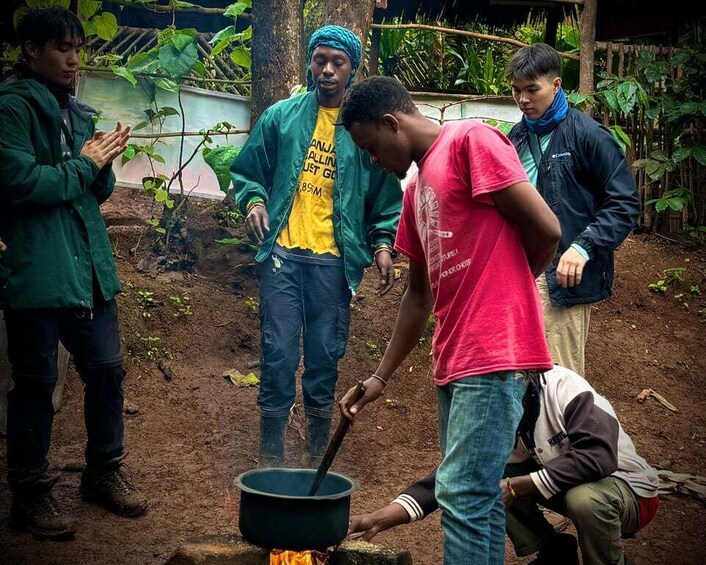 A group of people cooking outdoors with a pot over an open fire. 1