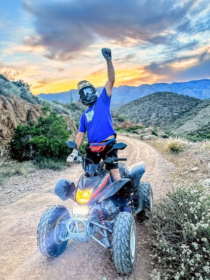A person riding a quad bike on a dirt road with mountains in the background. 2