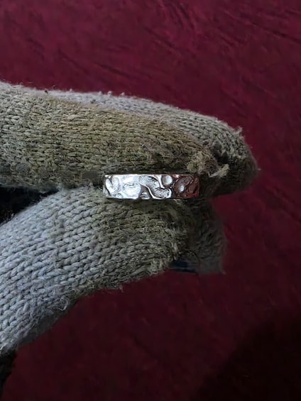 A metallic ring with intricate designs held by a gloved hand against a red background. 4