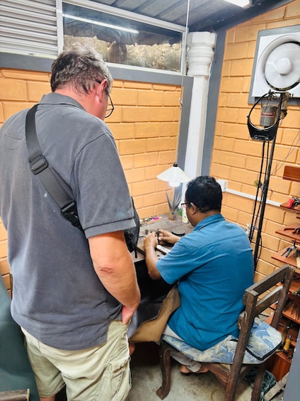 Two men working on a mechanical device, one standing and one seated at a workbench. 3