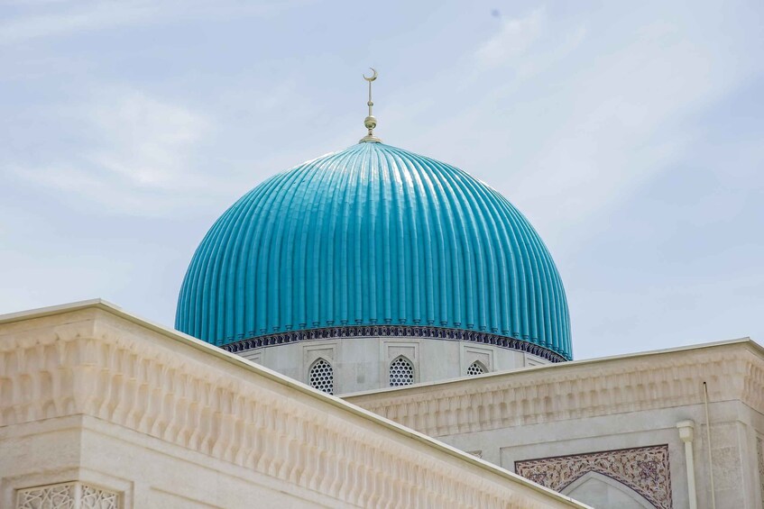 A large turquoise dome with a crescent moon finial, set against a clear sky. 1