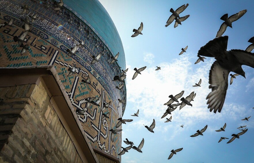 A mosque with intricate tile work and a dome, surrounded by flying birds. 2