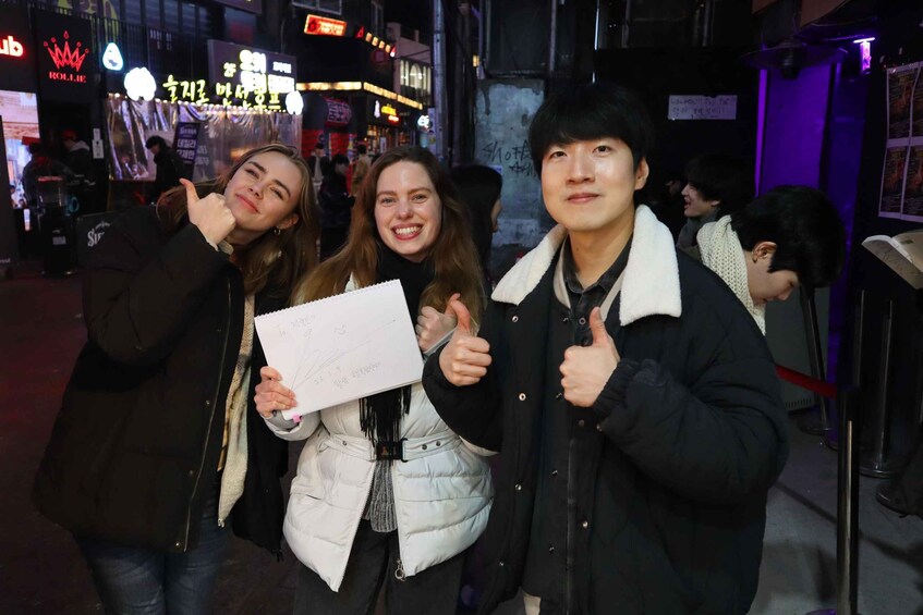 Three people in a city street at night, one holding a piece of paper. 3