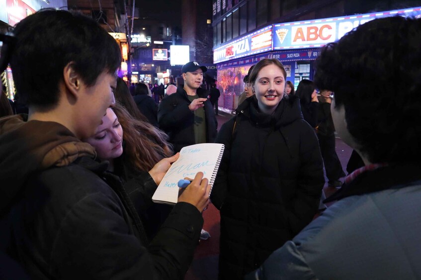 A group of people in a busy urban area at night, with illuminated signs and storefronts in the background. 4