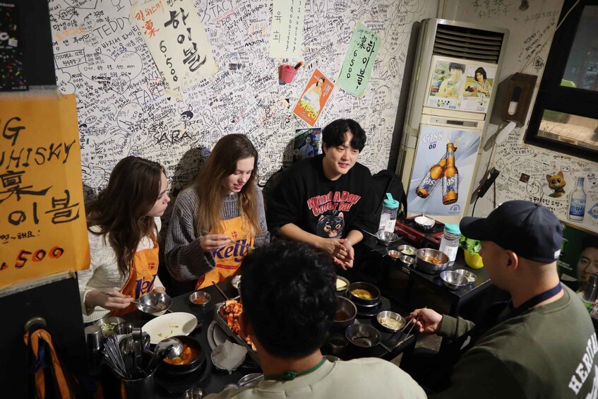 A group of people dining at a restaurant with a wall covered in various writings and drawings. 2