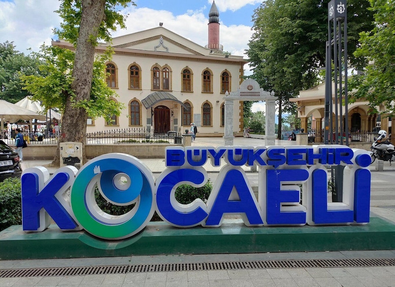 A large sign with the text 'BUYUKSEHIR KOCAELI' in front of a building with a clock tower. 1