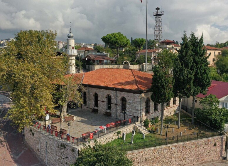 A stone building with a red-tiled roof, a bell tower, and a flagpole. 3