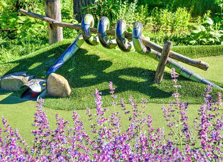A garden with a decorative metal sculpture, a wooden post, and purple flowers. 1