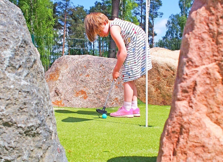 A person playing mini-golf on a green artificial turf with a putting green and a flagstick. 5
