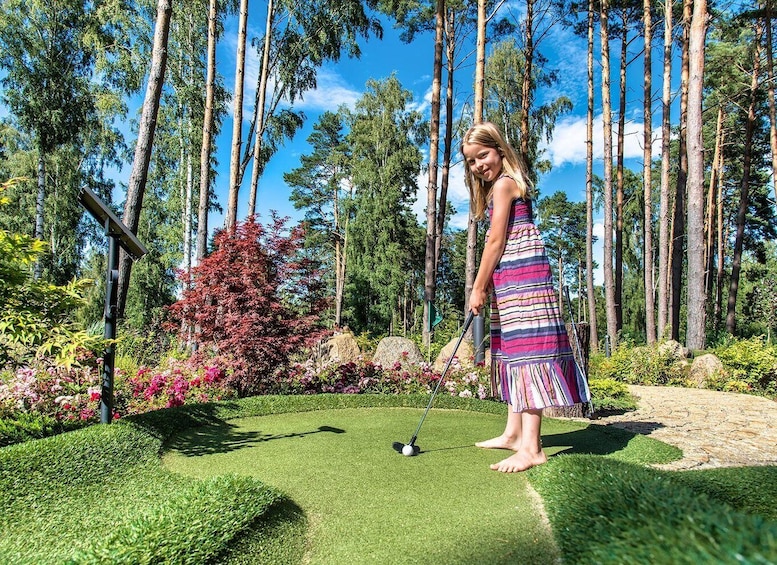 A person playing golf on a manicured course surrounded by tall trees and colorful foliage. 4