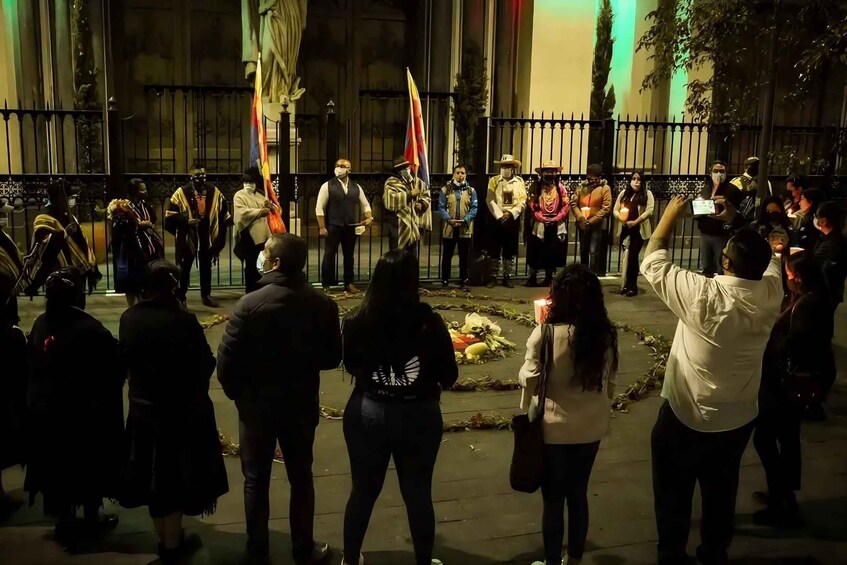 A nighttime outdoor gathering with people holding flags and candles, standing in a line. 2